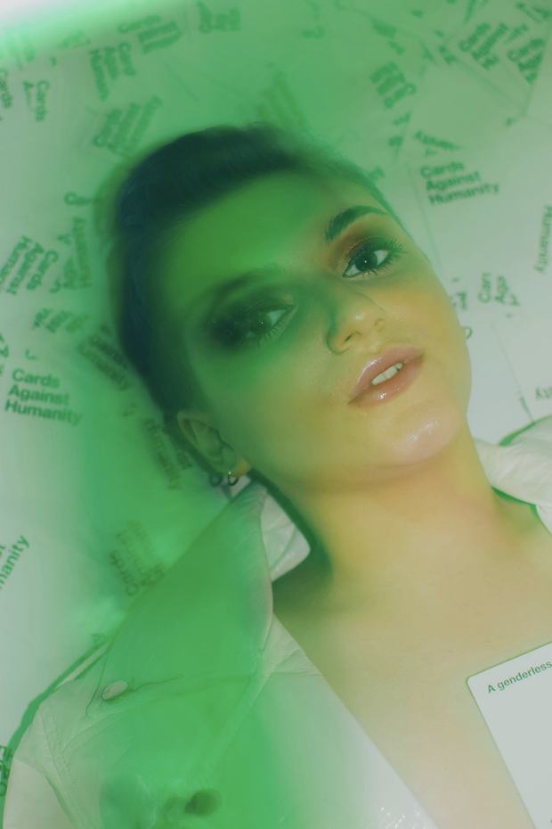 Laine lying on a scatter of cards under green light