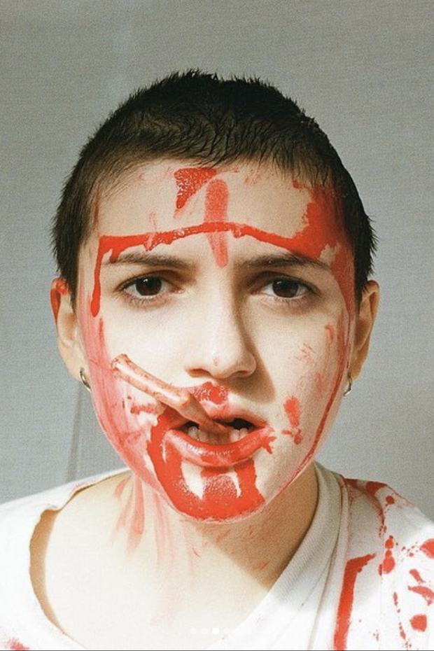 Laine looking straight to camera, face marked with red paint, from a portrait shoot